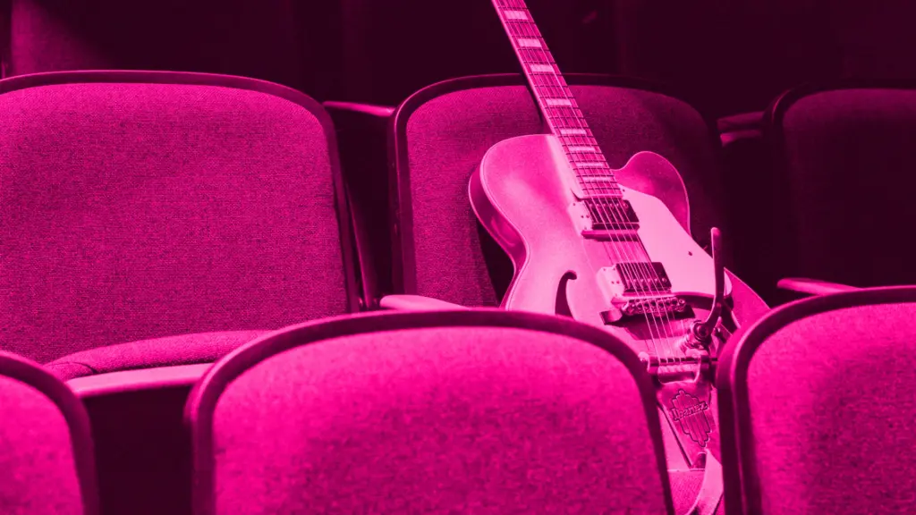 Electric guitar on a seat in concert hall, pink tint.